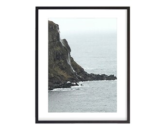 以下が含まれることがあります： 崖の側面を流れ落ちる滝のある岩場の崖の写真。崖は、背景に海のある海岸線にあります。水は濃い青色で、空は曇っています。