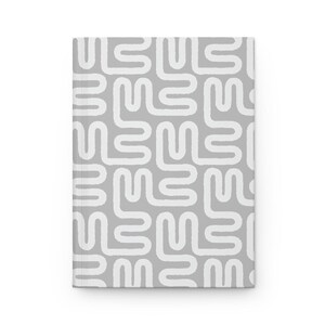 Puede incluir: Un cuaderno de tapa dura con fondo gris y un patr&oacute;n abstracto blanco. El patr&oacute;n consiste en formas redondeadas interconectadas. El cuaderno es rectangular y parece nuevo.