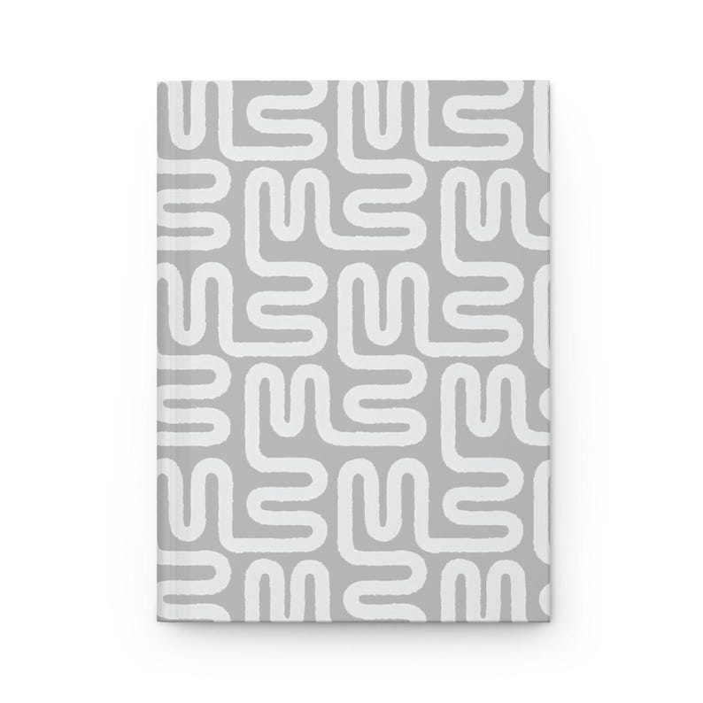Puede incluir: Un cuaderno de tapa dura con fondo gris y un patr&oacute;n abstracto blanco. El patr&oacute;n consiste en formas redondeadas interconectadas. El cuaderno es rectangular y parece nuevo.