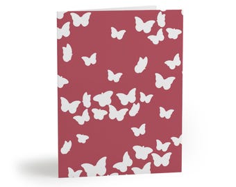 May include: A folded greeting card featuring a deep red background covered in a repeating pattern of solid white butterfly silhouettes of varying sizes scattered across the front surface of the card in a random orientation.