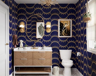 May include: A stylish bathroom with a navy blue and gold patterned wallpaper. The room features a wooden vanity with a marble countertop, a white toilet, and gold accents, including a light fixture and mirror. A framed art piece hangs on the wall, and a plant hangs from the ceiling.