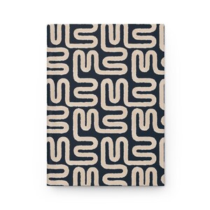 Puede incluir: Un cuaderno de tapa dura con un patr&oacute;n repetitivo de formas abstractas beige sobre un fondo azul marino. El dise&ntilde;o cubre toda la parte delantera del cuaderno, creando una est&eacute;tica cohesiva y visualmente atractiva.