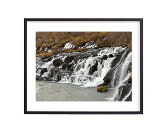 May include: A cascading waterfall flows over dark, moss-covered rocks. The water is white and foamy, creating a dramatic contrast against the dark rocks.