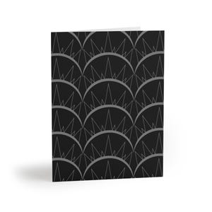 May include: A folded greeting card featuring a repeating pattern of dark gray semicircles on a black background. Each semicircle contains a series of thin, pointed triangular lines that extend upward, creating a geometric, crown-like motif across the surface.