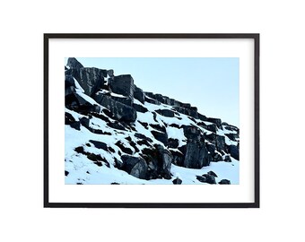 May include: A rocky mountainside covered in snow. The rocks are dark gray and the snow is white. The sky is a light blue.