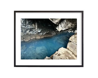 May include: A close-up view of a natural pool of turquoise blue water surrounded by dark gray rocks. The water is calm and clear, reflecting the light from above. The rocks are rough and textured, creating a contrast with the smooth surface of the water.