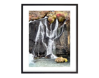 May include: A waterfall cascades down a rocky cliff face, creating a dramatic display of nature's power. The water flows in multiple streams, creating a unique and beautiful pattern. The surrounding vegetation adds a touch of color to the scene.