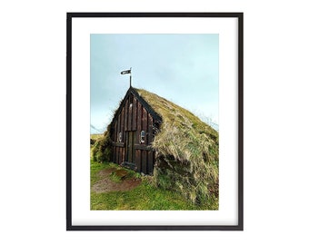 May include: A wooden house with a grass roof and a small flag on top. The house is surrounded by green grass and is set against a cloudy sky.