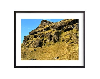 May include: A rocky hillside covered in green moss and grass, with a blue sky in the background.