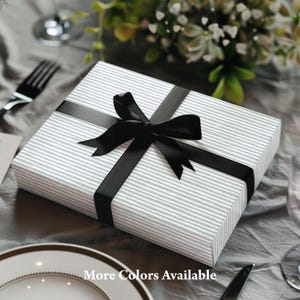 May include: A rectangular gift box wrapped in gray and white striped paper, tied with a black satin ribbon and bow. The text "More Colors Available" is printed on the bottom of the image.