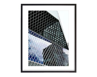 May include: A black and white photograph of a modern building with a geometric glass facade. The building is reflected in the glass panels, creating a pattern of overlapping squares.