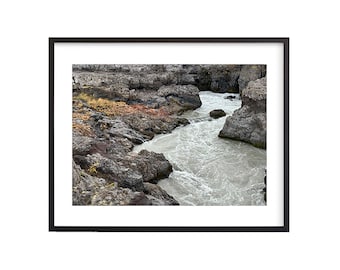 May include: A close-up of a rushing river flowing through a rocky canyon. The water is a milky white color and the rocks are a mix of gray, brown, and black.