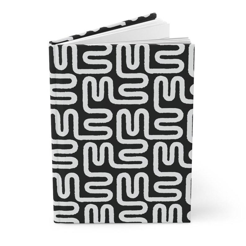 Puede incluir: Un cuaderno de tapa dura con un patr&oacute;n geom&eacute;trico en blanco y negro. El patr&oacute;n consiste en formas blancas, estilizadas e interconectadas sobre un fondo negro. El cuaderno est&aacute; abierto, revelando p&aacute;ginas blancas en blanco.