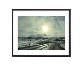 May include: A scenic view of a road winding through a snowy landscape with a bright sun shining through the clouds.