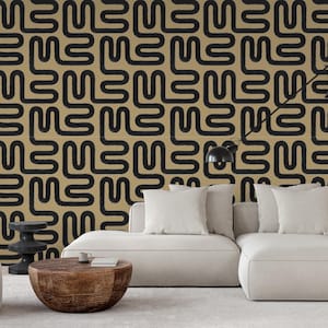 May include: A modern living room with a beige sectional sofa, a round wooden coffee table, and a patterned wallpaper. The wallpaper features a repeating black squiggly design on a tan background. A black lamp and a small side table are also visible.