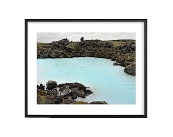 May include: A blue lagoon surrounded by black volcanic rock formations. The water is a vibrant blue and the rocks are covered in moss.