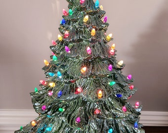 May include: A ceramic Christmas tree with a star topper and colorful lights. The tree is green with a textured surface and is lit with various colored bulbs. The star is clear and sits atop the tree.