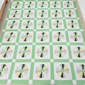 May include: A large, handmade quilt featuring a repeating pattern of colorful, circular designs. The quilt's primary colors are white and green, with accents of yellow, black, and patterned fabrics within the circles. The quilt is likely for a bed.