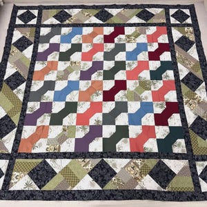 May include: A handmade quilt with a colorful patchwork design. The central section features a repeating pattern of bow tie shapes in various colors, including blue, red, and orange. The quilt is bordered with patterned fabric and a dark blue edge.