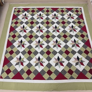 May include: A handmade quilt with a repeating pattern of star-shaped designs within diamond shapes. The quilt features a color palette of red, green, white, and various patterned fabrics. The border is a solid green with a white inner border.
