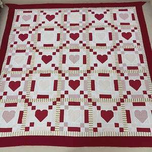 May include: A handmade quilt featuring a repeating pattern of red hearts on a white background. The hearts are solid or striped, with a red border and gold accents. The quilt is a square shape, perfect for a bed or wall hanging.