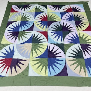 May include: A large, colorful quilt with a repeating sunburst pattern. The quilt features a variety of colors, including red, blue, green, yellow, and purple. The quilt is bordered with a solid green fabric.