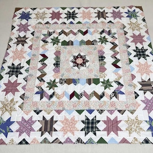 May include: Handmade quilt featuring a star pattern in various fabrics. The quilt showcases a central star design surrounded by multiple star blocks in shades of pink, green, blue, and brown, set against a white background. The quilt is a patchwork design.