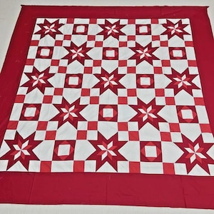 May include: A red, white, and red star-patterned quilt. The quilt features alternating star and square patterns in shades of red and white. The quilt has a solid red border.