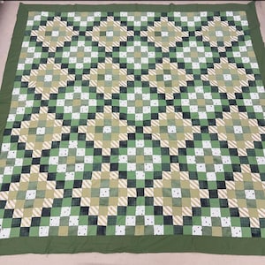 May include: A large, handmade quilt with a patchwork design. The quilt features a repeating pattern of squares in shades of green, white, and tan. The squares are arranged in a diagonal pattern, creating a visually interesting design. The quilt has a solid green border.