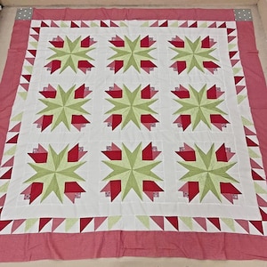 May include: A handmade quilt with a white center featuring nine starburst patterns with red and green floral designs. The quilt has a red border with triangle accents and a red backing.