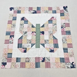 May include: A handmade patchwork quilt featuring a butterfly design. The quilt showcases a white center with a green checkered body and wings composed of various fabric squares in pink, blue, and floral patterns. The border is a mix of similar fabrics.