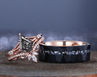May include: A pair of wedding bands. The engagement ring features a pear-shaped black diamond with a rose gold band and a delicate floral design. The wedding band is a black tungsten band with a rose gold inlay.