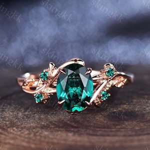 May include: A rose gold ring with a large oval emerald green gemstone surrounded by smaller emerald green gemstones set in a delicate vine design.
