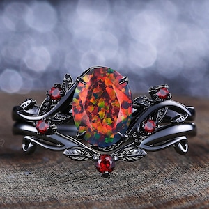 May include: Black ring with a large oval opal gemstone surrounded by smaller red gemstones and black metal leaves.