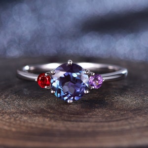 May include: A silver ring featuring a large, round, blue gemstone surrounded by smaller red and purple gemstones.