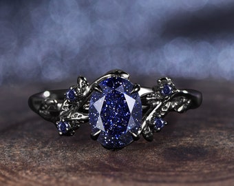 May include: A black ring with a large, oval-shaped blue gemstone set in a delicate, leafy design. The gemstone is a sparkly, dark blue color.