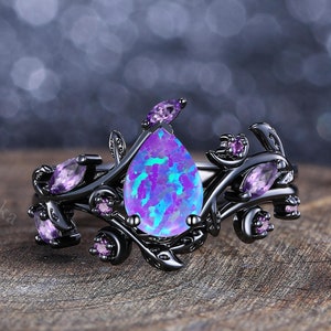May include: Black ring with a teardrop-shaped purple opal gemstone surrounded by smaller purple gemstones and black floral accents.