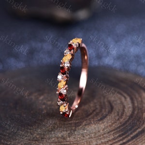 Könnte beinhalten: Ein zarter Goldring mit einer Reihe von abwechselnd roten, gelben und weißen Edelsteinen. Der Ring liegt auf einer Holzoberfläche.