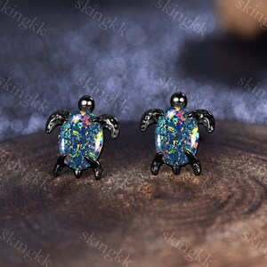 May include: A pair of black turtle earrings with iridescent opal stones. The earrings are small and delicate, and the opal stones are a beautiful blue and green color.