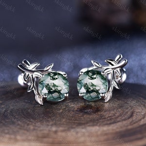 May include: A pair of silver earrings with green moss agate stones and a delicate branch design.