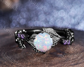 May include: Black ring with a white opal gemstone surrounded by leaf-shaped details. Two small purple gemstones are set on the band.