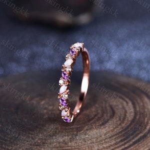 May include: A rose gold band ring with a delicate design featuring alternating oval-shaped opals and amethyst gemstones.