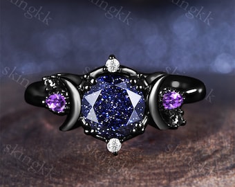 Puede incluir: Anillo negro con una piedra preciosa azul rodeada de pequeñas piedras preciosas blancas. El anillo presenta dos diseños de luna creciente a cada lado de la piedra preciosa, cada uno con una pequeña piedra preciosa púrpura.