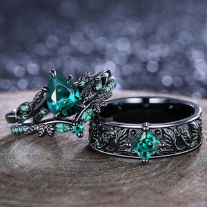 Peut inclure: Deux bagues noires avec des pierres précieuses vert émeraude. L'une des bagues présente une pierre en forme de poire et des motifs de feuilles. L'autre bague a une pierre carrée et un motif de feuilles.