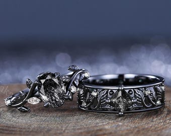 May include: A black and white diamond engagement ring set with a black diamond center stone and a matching wedding band. The rings feature a delicate floral design with leaves and small diamonds.