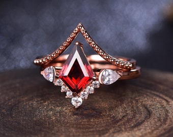 May include: A rose gold ring with a large, red, faceted gemstone surrounded by smaller, clear gemstones. The ring has a delicate, pointed design.