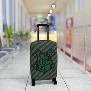 May include: A green and gray striped suitcase with a black Hogwarts crest logo. The crest features a shield with a lion, eagle, badger, and snake.