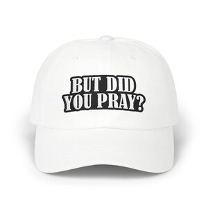 Könnte beinhalten: Eine weiße Baseballkappe mit dem gestickten Text "BUT DID YOU PRAY?" in Schwarz. Die Kappe hat einen gebogenen Schirm und ein klassisches Sechs-Panel-Design. Der Text ist in einer fetten, blockartigen Schriftart gehalten. Ein lässiges Accessoire.
