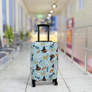 May include: A blue suitcase with a Harry Potter themed design. The suitcase is covered in a pattern of owls, wands, and the Hogwarts crest. The suitcase has a black handle and wheels.
