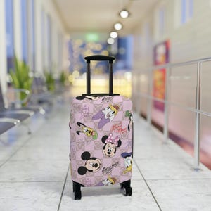 May include: A pink suitcase with a black handle and wheels, decorated with a pattern of Disney characters such as Mickey and Minnie Mouse, Donald Duck, and Goofy. The design is set against a checkered background.